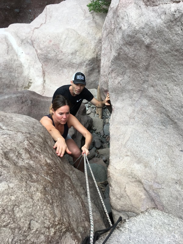 Two hikers navigating a rope through a narrow boulder gap in the canyons near Loreto