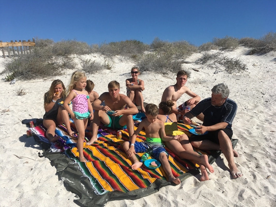Large family enjoying a beach picnic on colorful Mexican blankets on a white sand island beach near Loreto