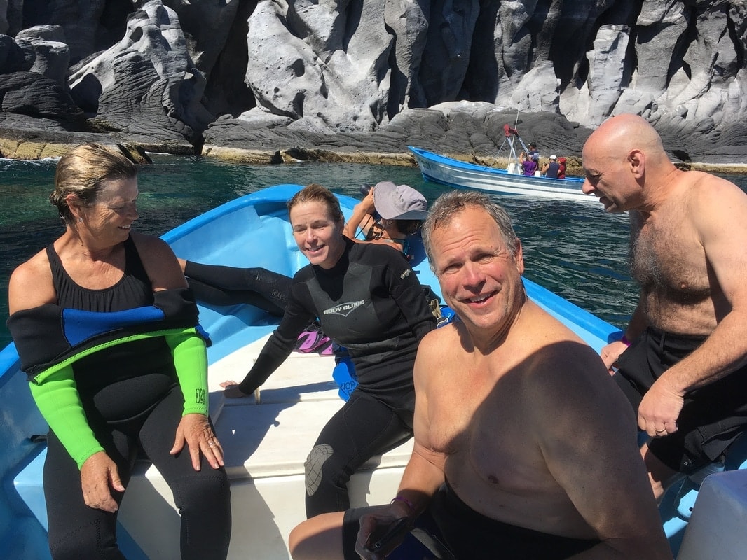 Four guests in wetsuits relaxing on a blue panga inside a dramatic volcanic cave cove on a Loreto island snorkeling tour