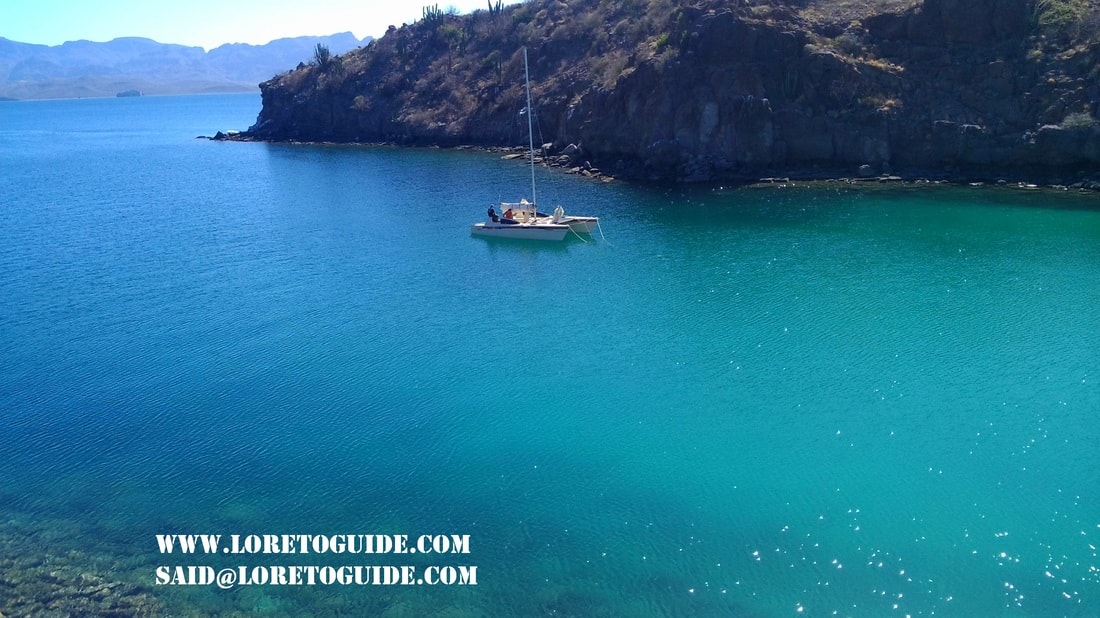 Sailboat anchored in a glassy turquoise cove beneath volcanic cliffs near Loreto