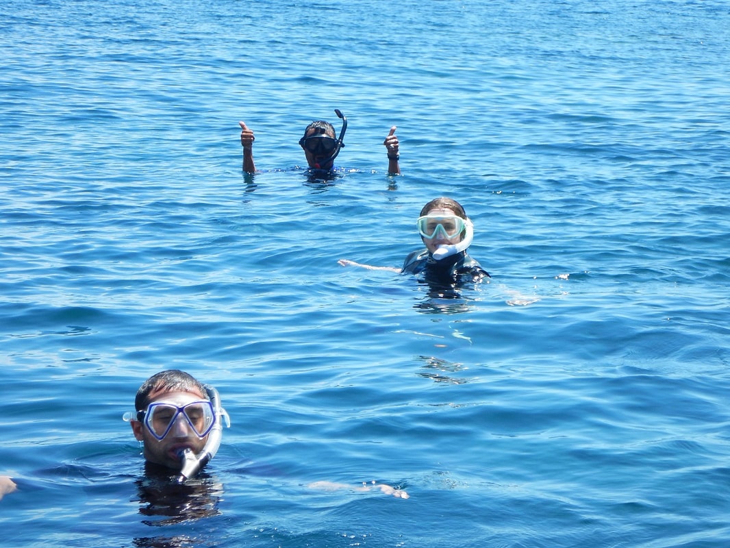 Guide giving double thumbs up and two guests floating in open blue water during a Loreto island snorkeling tour